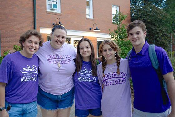 A group of students in various purple ChathamU t-shirts smile and pose for a photo at Orientation